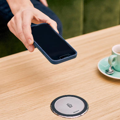 Disq wireless charger has been integrated to a coffee table. A person is placing their phone down to charge.